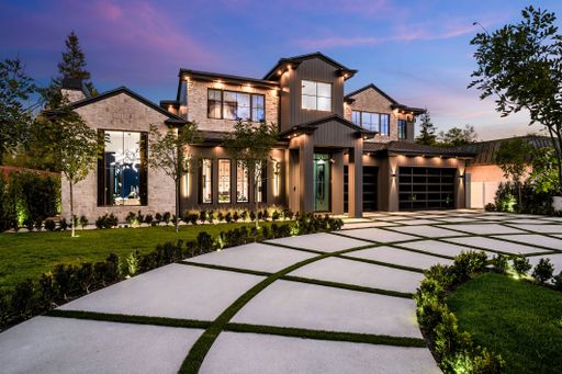 Modern luxury home exterior with a beautifully landscaped front yard and driveway at dusk.