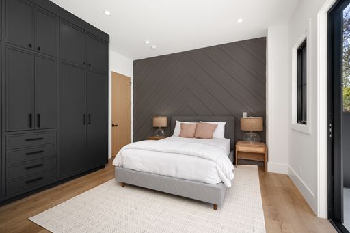Modern bedroom with dark built-in wardrobes, a cozy bed, and wooden side tables, featuring a chevron-patterned accent wall and natural light.