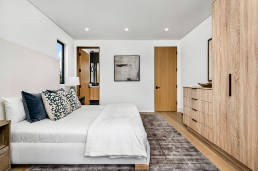 Modern bedroom interior with wooden furniture, white bedding, and decorative pillows, featuring a minimalist design and natural light.