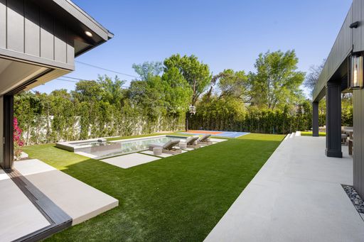A modern backyard with a swimming pool, lounge chairs, and a basketball court surrounded by lush greenery.