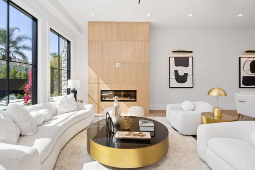 Modern living room with large windows, contemporary furniture, and a fireplace, featuring abstract art and a view of the garden.