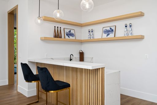 Modern home interior with a stylish bar area, featuring a marble countertop, wooden shelves, and elegant decor.