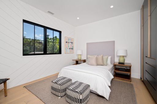 Modern bedroom interior with a large window, double bed, nightstands, and decorative stools.