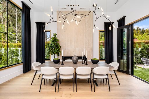 Modern dining room interior with a large table, stylish chandelier, and floor-to-ceiling windows overlooking a lush garden.