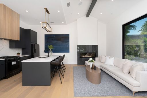 Modern open-concept kitchen and living room with minimalist design, featuring black cabinets, white countertops, and a cozy white sofa.