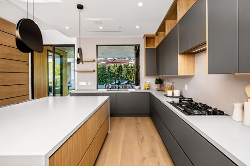 Modern kitchen interior with sleek cabinets, large island, and outdoor view through glass doors.