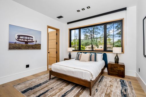 Modern bedroom interior with a large window, wooden furniture, and a stylish rug, featuring a scenic outdoor view.