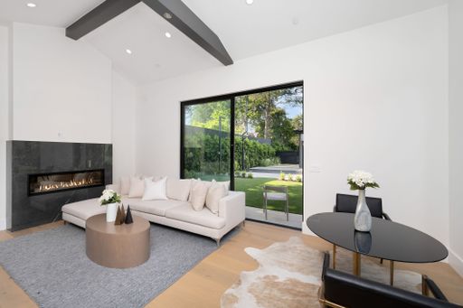 Modern living room with a fireplace, large windows, and minimalistic furniture leading to a garden area.