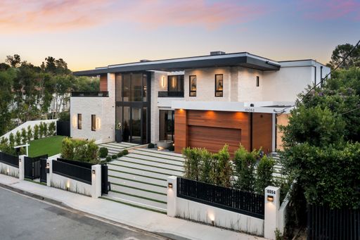 Modern luxury house exterior at sunset with green lawn and driveway in a suburban neighborhood.
