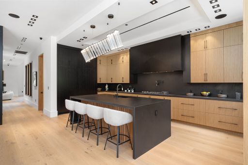 Modern kitchen interior with wooden cabinets, black countertops, and a central island with bar stools, featuring contemporary lighting fixtures.
