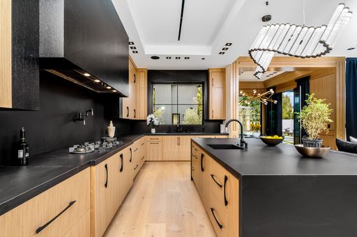 Modern kitchen interior with wooden cabinets, black countertops, and unique lighting fixtures, featuring an island and large windows.