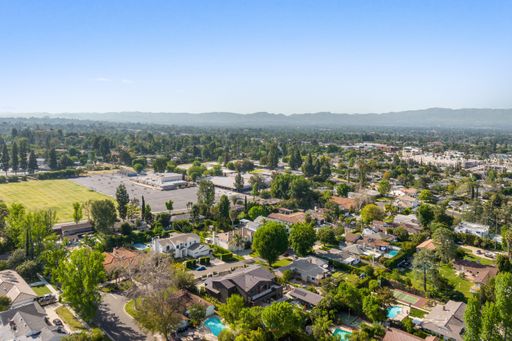 Aerial view of a suburban neighborhood with houses, trees, and a school field on a clear day.