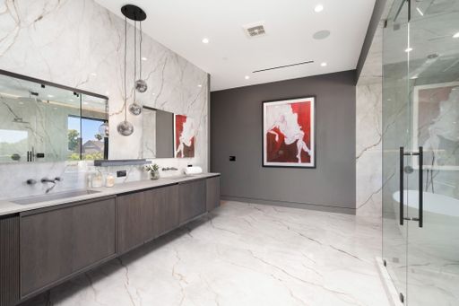 Modern bathroom interior with marble walls and floor, double sink vanity, glass shower, and contemporary artwork.