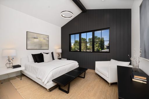 Modern bedroom interior with black accent wall, white bed, and large window offering outdoor view.