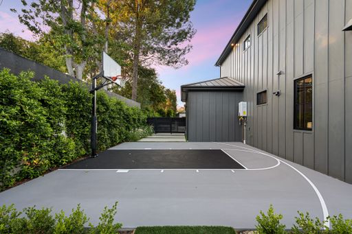 A modern residential backyard with a basketball court, surrounded by lush greenery and a contemporary house.