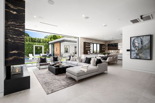 Modern open-plan living room with large windows, contemporary furniture, and view of a lush garden and pool area.