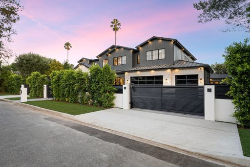 Modern luxury home exterior with a black gate, lush greenery, and a beautiful sunset sky in a suburban neighborhood.