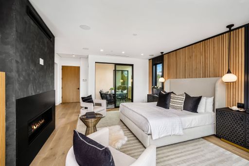 Modern bedroom with a cozy fireplace, stylish decor, and wooden accents, featuring a large bed, comfortable chairs, and natural light.
