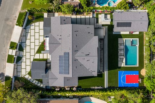 Aerial view of a modern house with a pool, basketball court, and landscaped yard in a suburban neighborhood.