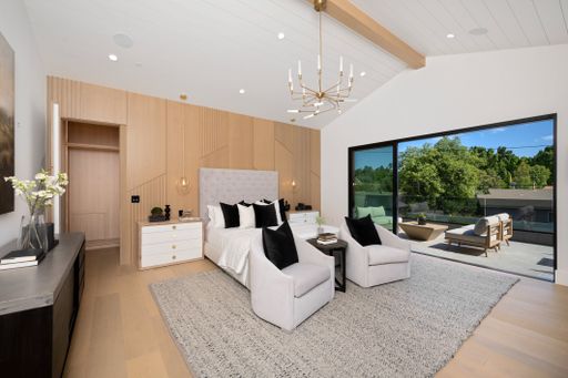 Modern bedroom with stylish furniture, large window, and outdoor patio view in a luxurious home.