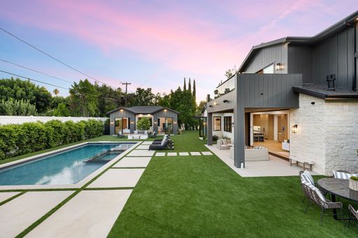 A modern backyard with a swimming pool, patio area, and contemporary house at sunset.