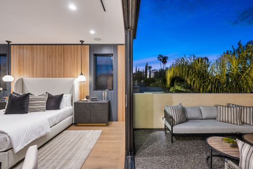 Modern bedroom with wooden wall paneling and an adjacent outdoor seating area, captured during twilight.