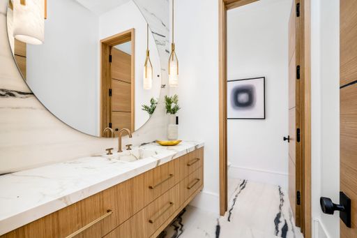 Modern bathroom interior with marble countertop, wooden cabinets, round mirror, pendant lights, and contemporary decor.