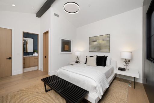 Modern minimalist bedroom with white walls, wooden floor, black bench, and contemporary decor.