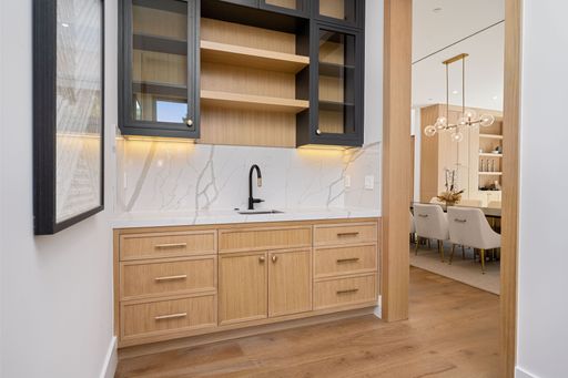 Modern kitchen interior with wooden cabinets, marble backsplash, and a black faucet, leading to a dining area with elegant decor.