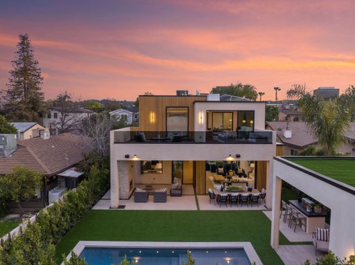 A modern two-story house with a pool and outdoor seating area at sunset in a suburban neighborhood.