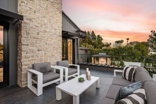 Modern outdoor patio with stylish furniture and a scenic sunset view, featuring a stone wall and lush greenery.