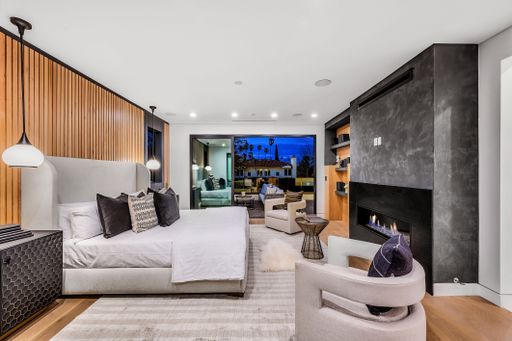 Modern bedroom interior with wooden accents, fireplace, and large windows overlooking a cityscape at dusk.