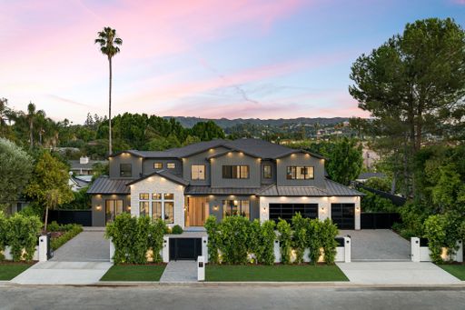 Modern luxury house with a beautiful garden and sunset sky in the background, located in a suburban neighborhood.