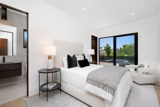 Modern bedroom with a large window, a neatly made bed, and a connected bathroom with contemporary design.