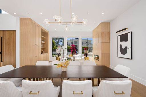 Modern dining room with elegant furniture, contemporary lighting, and a view of a bright living area with large windows and vibrant decor.