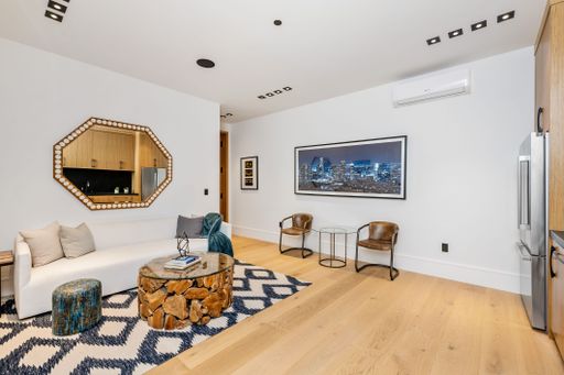 Modern living room with stylish furniture, wooden flooring, and contemporary decor, featuring a large wall mirror and cityscape artwork.