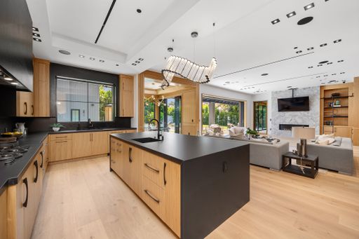 Modern open-concept kitchen and living room with wooden cabinetry, large island, and contemporary lighting in a luxury home.