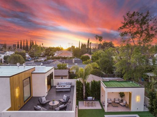 Aerial view of a modern house with rooftop terrace and backyard patio at sunset in a suburban neighborhood.