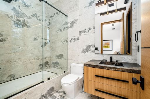 Modern bathroom interior with a glass shower, marble walls, and a wooden vanity with a large mirror.