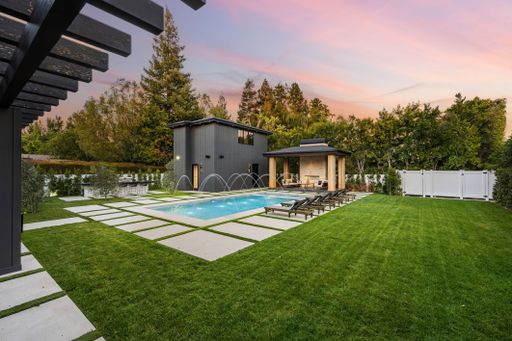 Modern backyard with a swimming pool, lounge chairs, and a pergola at sunset.