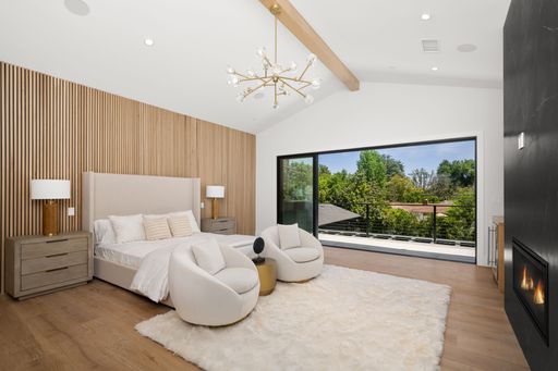 Modern bedroom with wooden accent wall, cozy seating, and large window offering a scenic view.