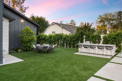 Modern backyard with outdoor dining area and bar counter, surrounded by greenery and a beautiful sunset sky.