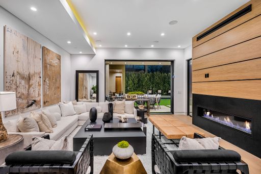 Modern living room with contemporary furniture, large artworks, and a fireplace, opening to an outdoor patio area.