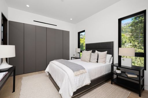 Modern bedroom interior with a large bed, gray wardrobe, and natural light from windows overlooking greenery