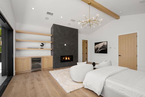 Modern bedroom with fireplace, wooden floor, white bed, and contemporary lighting.