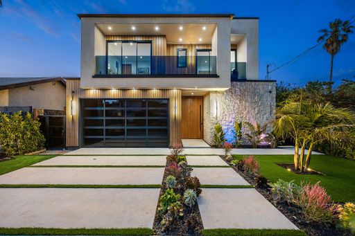 Modern two-story house with a well-lit exterior and landscaped front yard featuring palm trees and succulents.