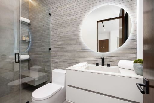 Modern bathroom interior with a large round mirror, sleek white vanity, and glass shower enclosure.