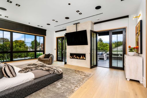 Modern bedroom interior with large windows, fireplace, and access to an outdoor patio. Features contemporary decor and natural light.