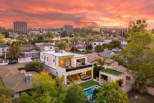 Aerial view of a modern house with a swimming pool and lush greenery at sunset in a suburban neighborhood.