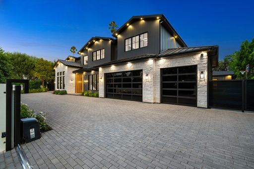 Modern luxury house with a spacious driveway and well-lit exterior during twilight, showcasing contemporary architecture and landscaping.